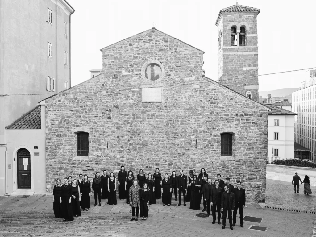 Group photo of the choir with conductor Petra grassi and pianist Martina Salateo in front of a church